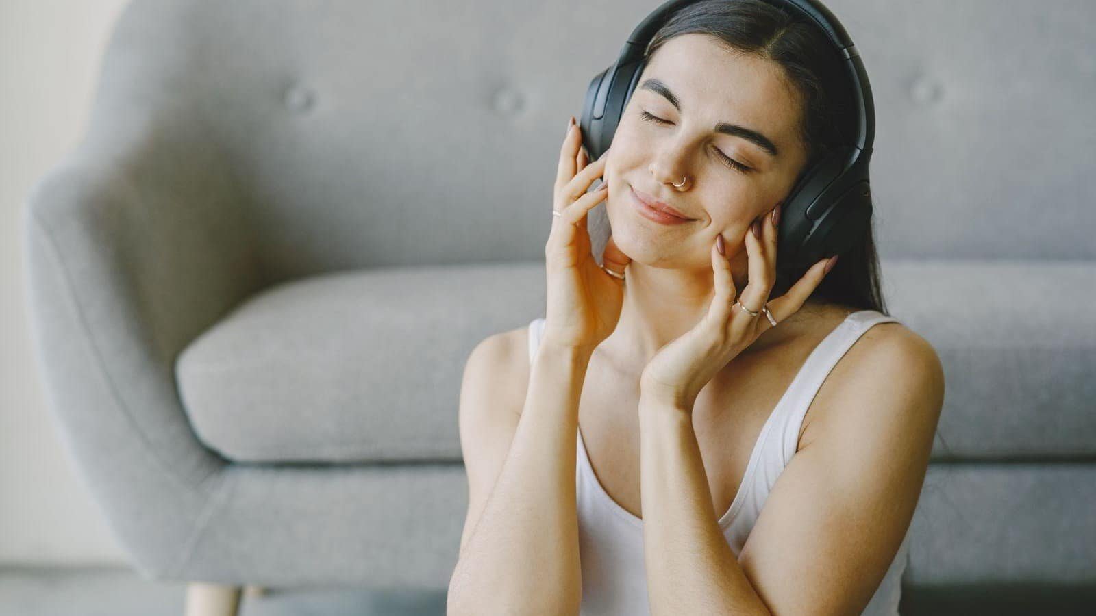 Mujer con auriculares descansando junto a un sofá.