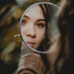 Mujer observando su reflejo en un espejo de mano, imagen ilustrativa sobre identidad.